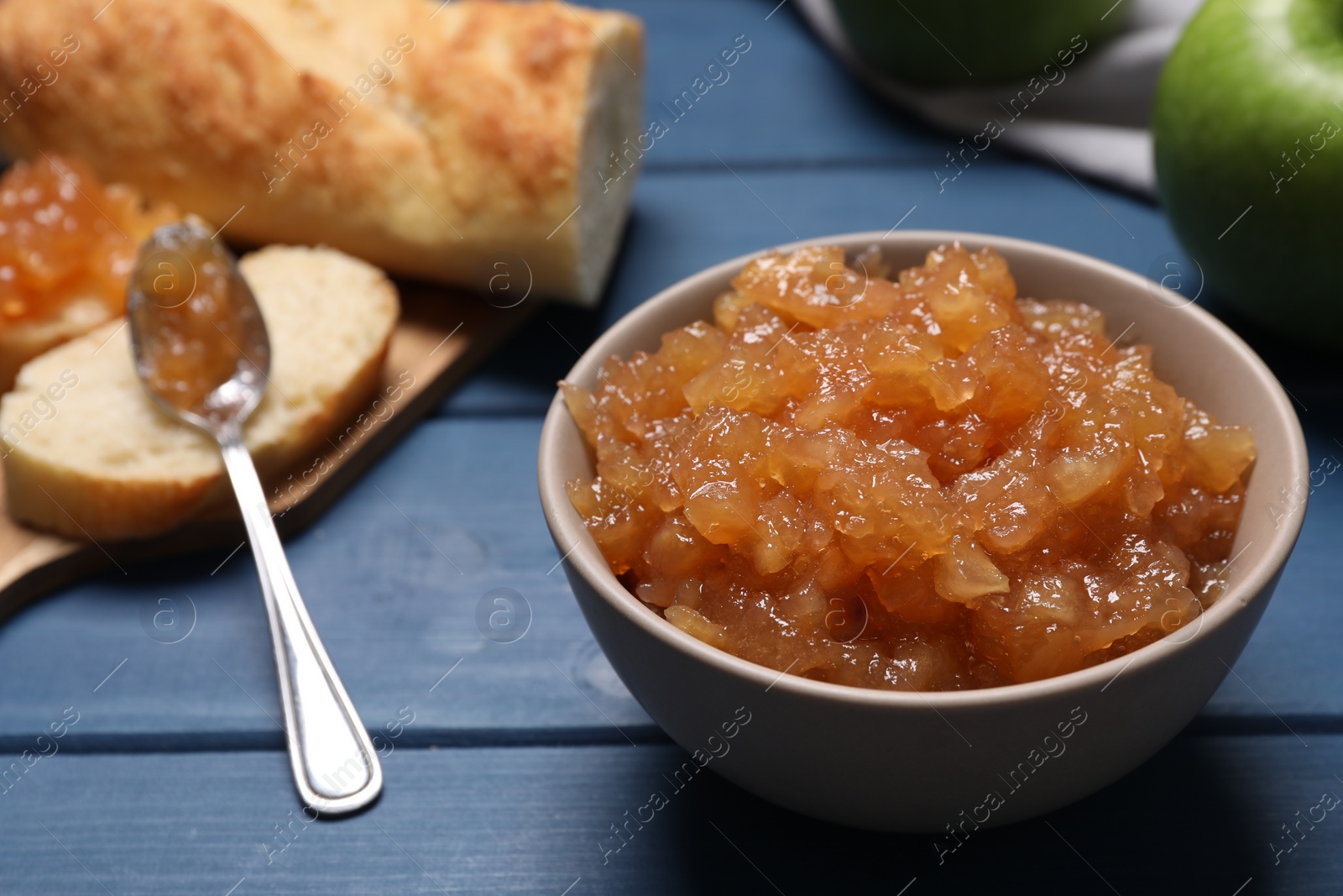 Photo of Bowl with delicious apple jam on blue wooden table, closeup