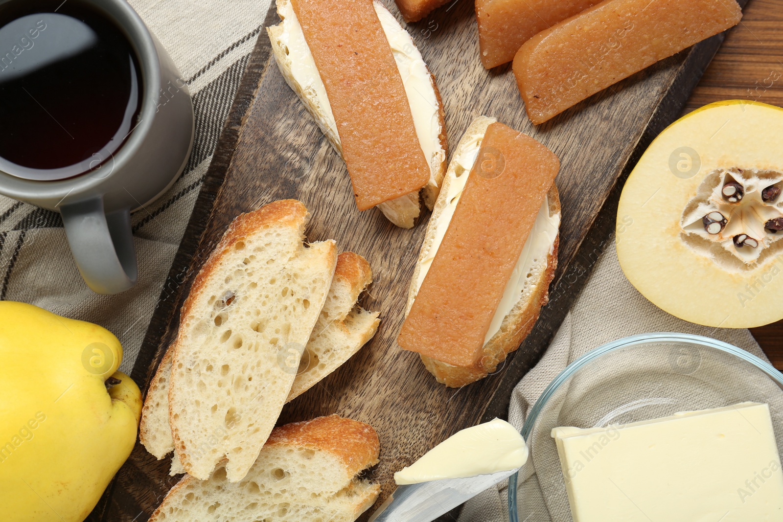 Photo of Delicious quince paste, bread, butter, cup of tea and fresh fruits on wooden table, flat lay