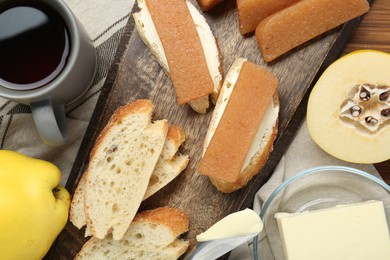 Photo of Delicious quince paste, bread, butter, cup of tea and fresh fruits on wooden table, flat lay