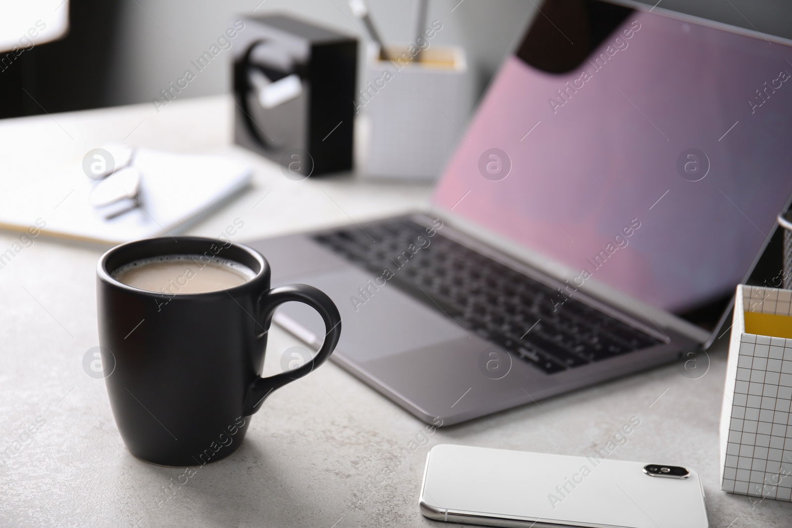 Photo of Black cup with coffee near laptop on office table. Break time