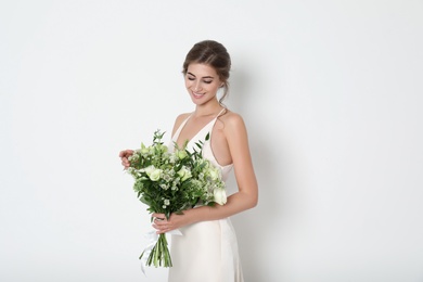 Young bride wearing wedding dress with beautiful bouquet on light background