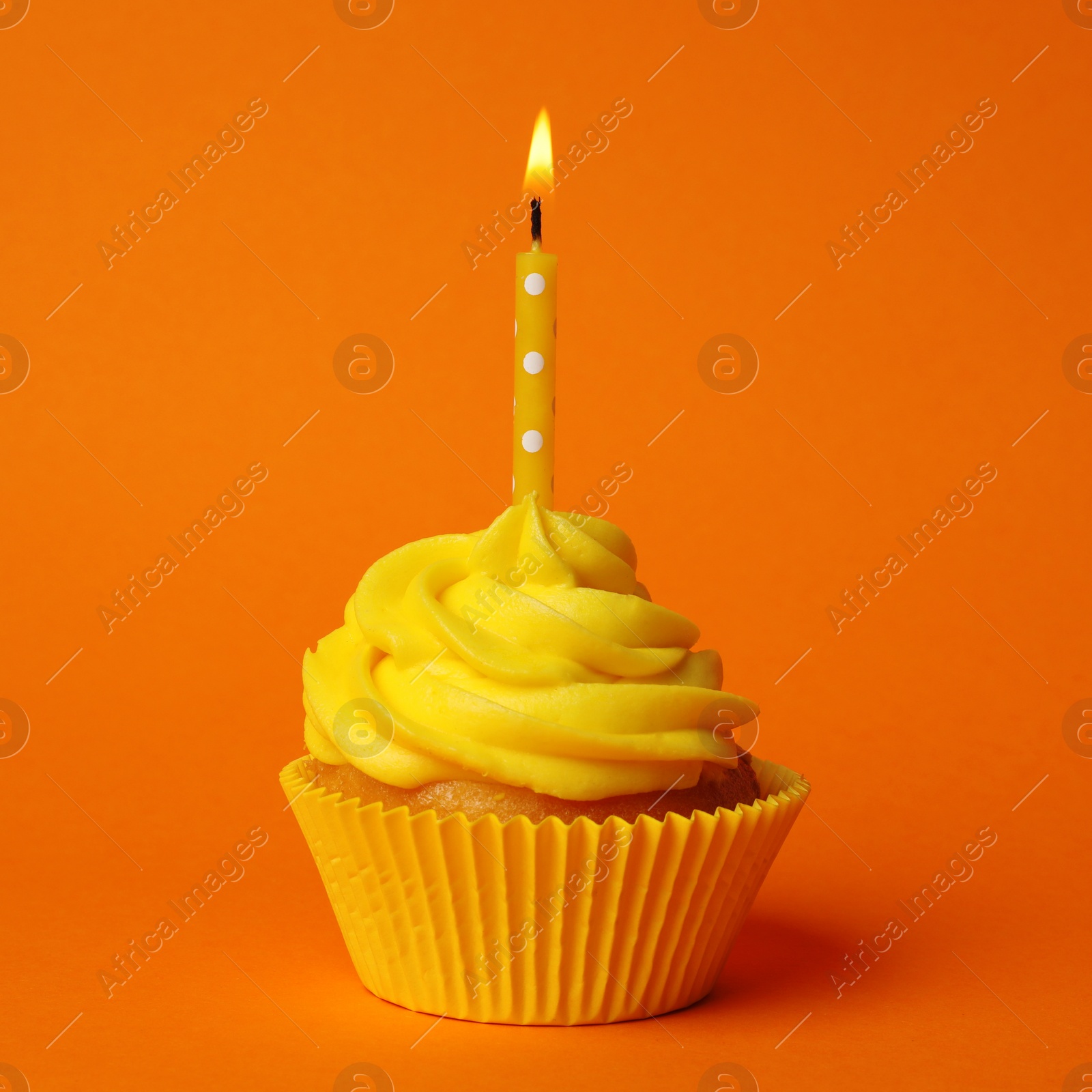 Photo of Delicious birthday cupcake with yellow cream and burning candle on orange background