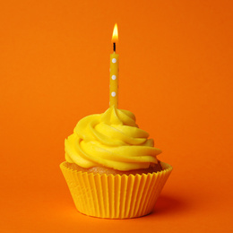 Delicious birthday cupcake with yellow cream and burning candle on orange background