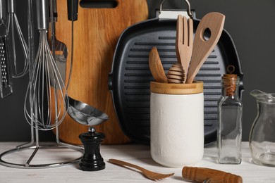 Set of different kitchen utensils on white wooden table against grey background