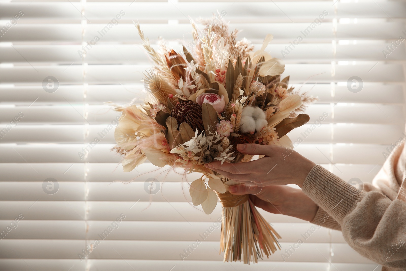 Photo of Woman holding beautiful dried flower bouquet near window at home, closeup