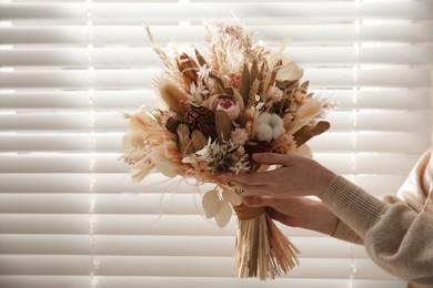 Photo of Woman holding beautiful dried flower bouquet near window at home, closeup