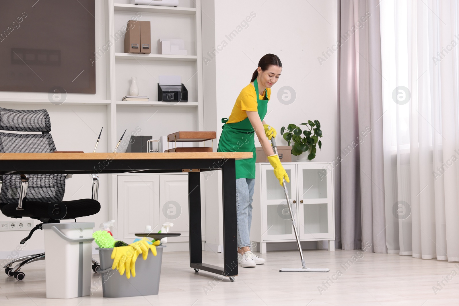 Photo of Cleaning service worker washing floor with mop. Bucket with supplies in office