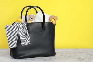 Photo of Mother's bag with baby's stuff on white marble table against yellow background. Space for text