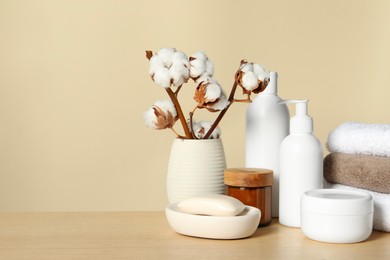 Photo of Different bath accessories and cotton flower on wooden table against beige background. Space for text