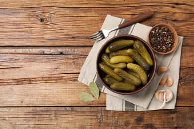 Photo of Tasty pickled cucumbers in bowl, fork and ingredients on wooden table, flat lay. Space for text