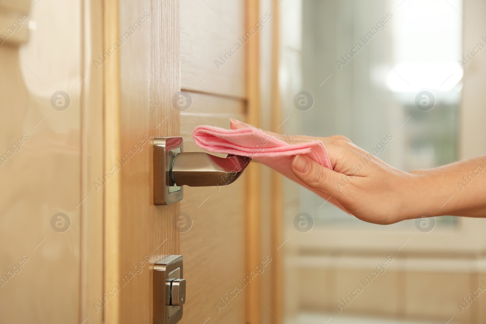 Photo of Woman cleaning door handle with rag indoors, closeup