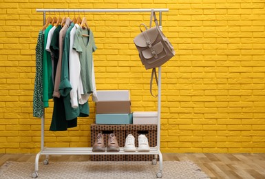 Rack with different stylish clothes and shoes indoors. Space for text