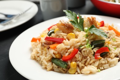 Delicious rice pilaf with chicken and vegetables on black table, closeup