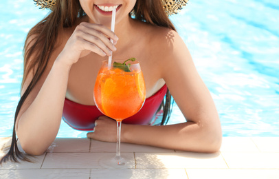 Photo of Woman with glass of refreshing drink in swimming pool, closeup