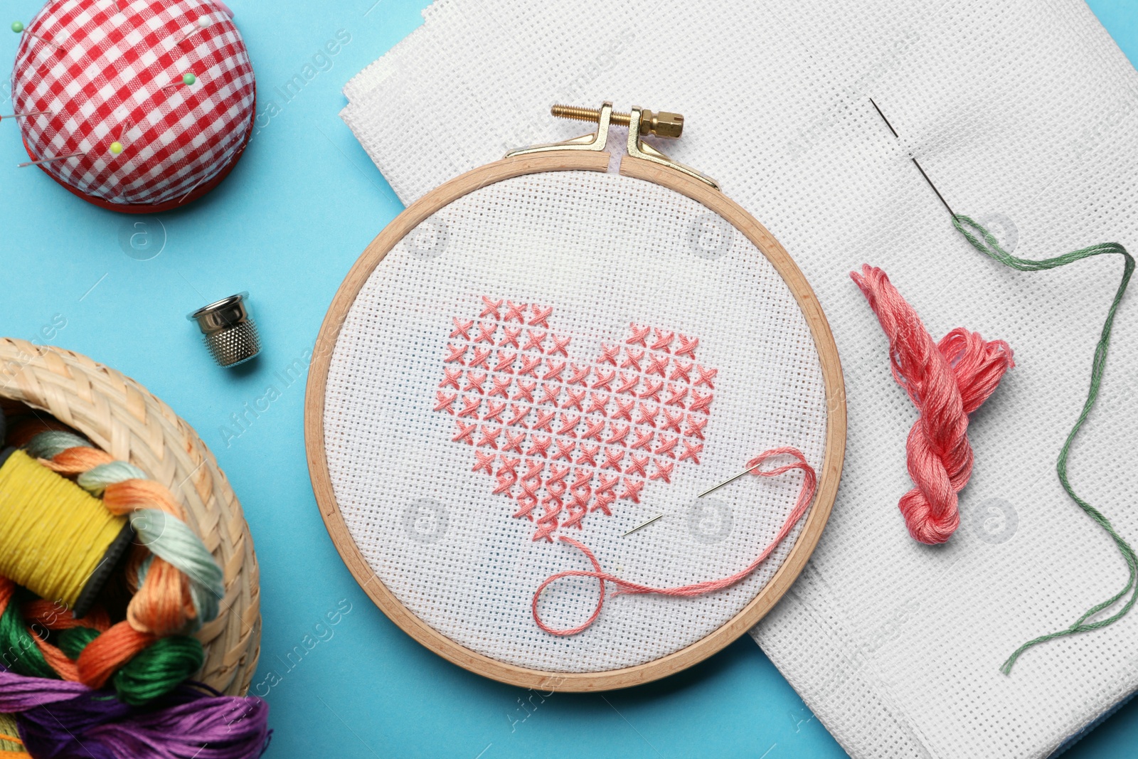 Photo of Flat lay composition with embroidery and different sewing accessories on light blue background