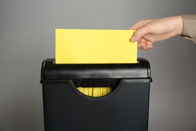 Photo of Woman destroying sheet of yellow paper with shredder on grey background, closeup