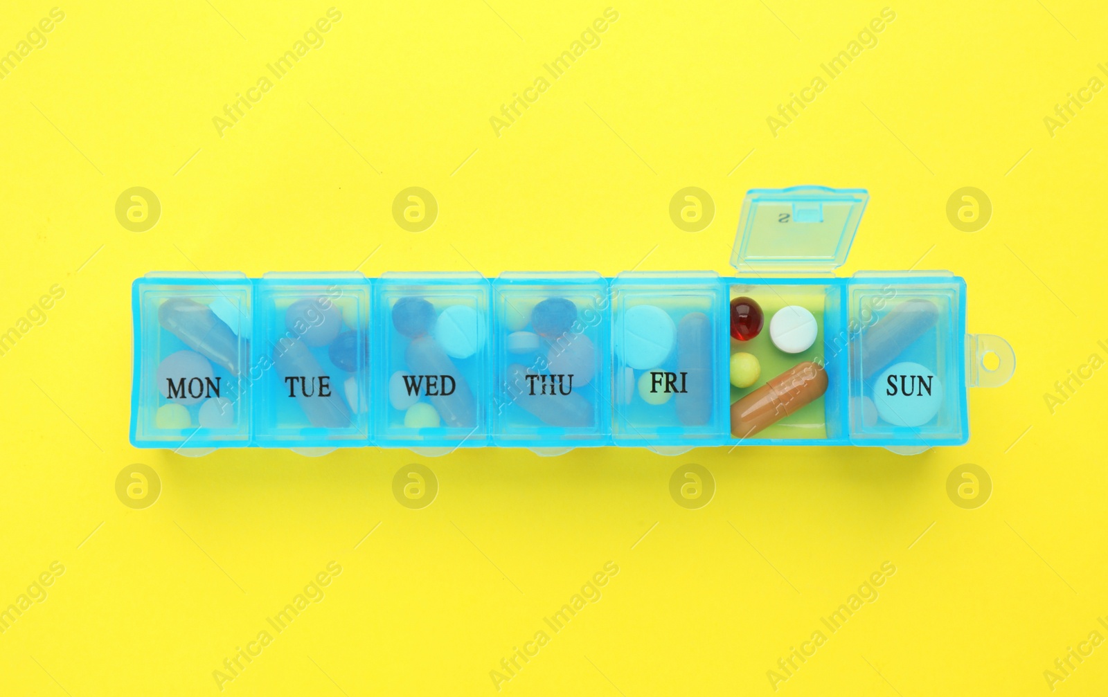 Photo of Pill box with medicaments on yellow background, top view