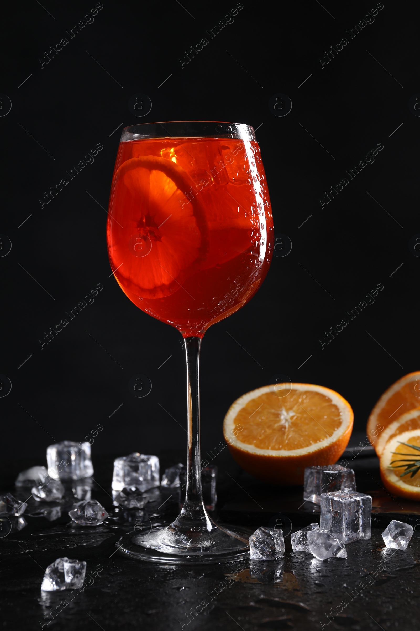 Photo of Glass of tasty Aperol spritz cocktail with orange slices and ice cubes on table against black background