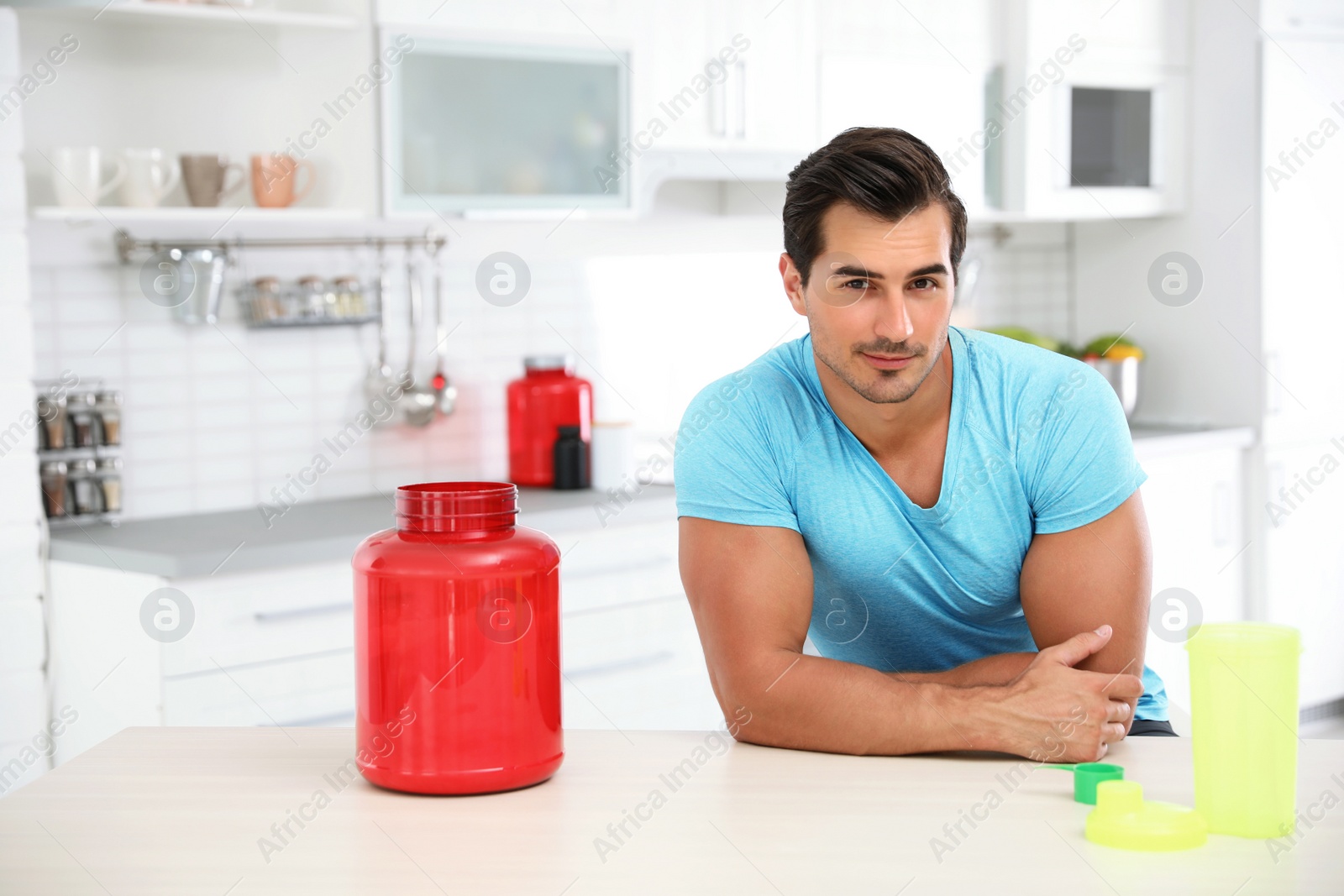 Photo of Young athletic man with protein shake powder in kitchen