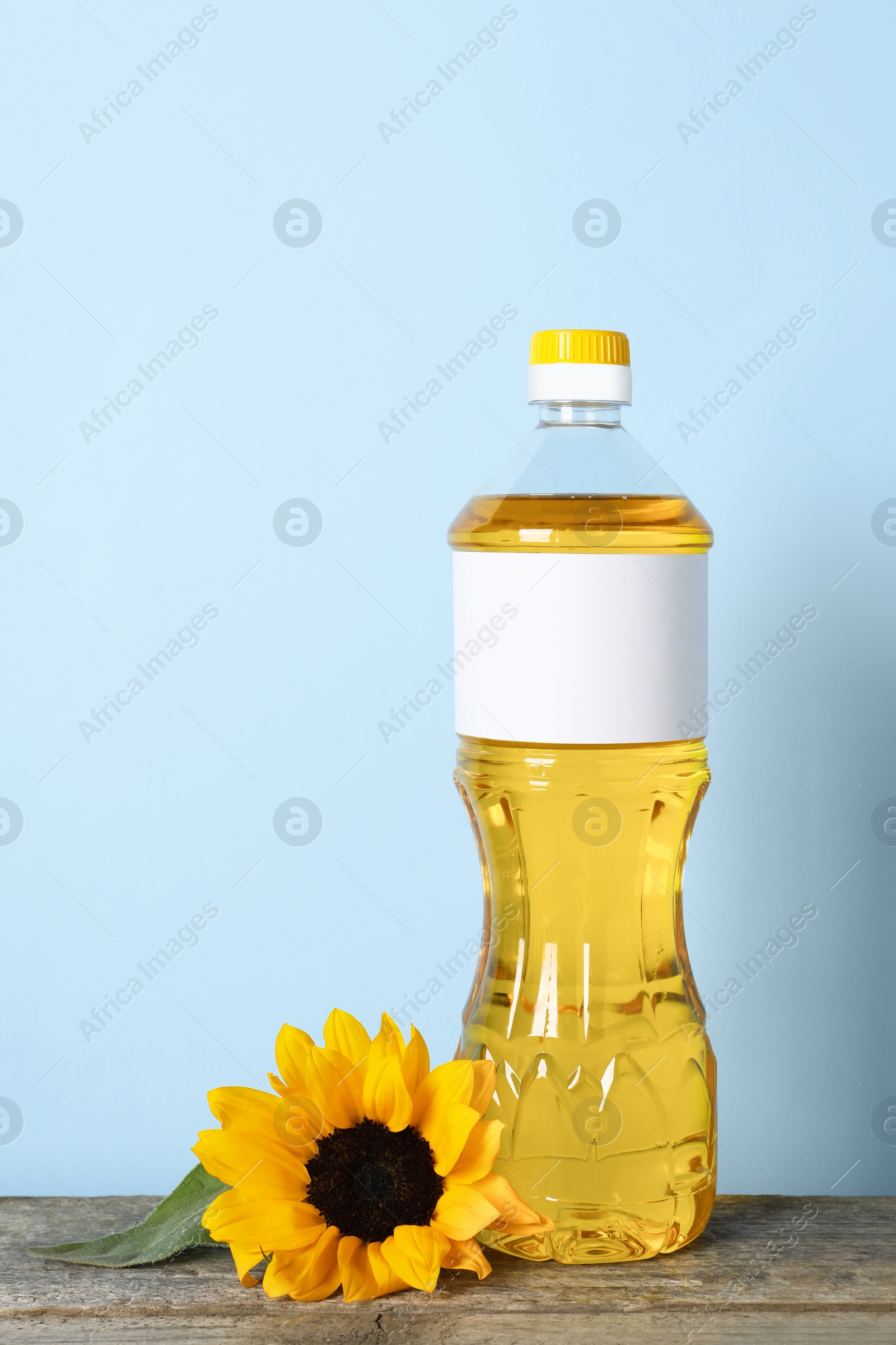 Photo of Bottle of cooking oil and sunflower on wooden table