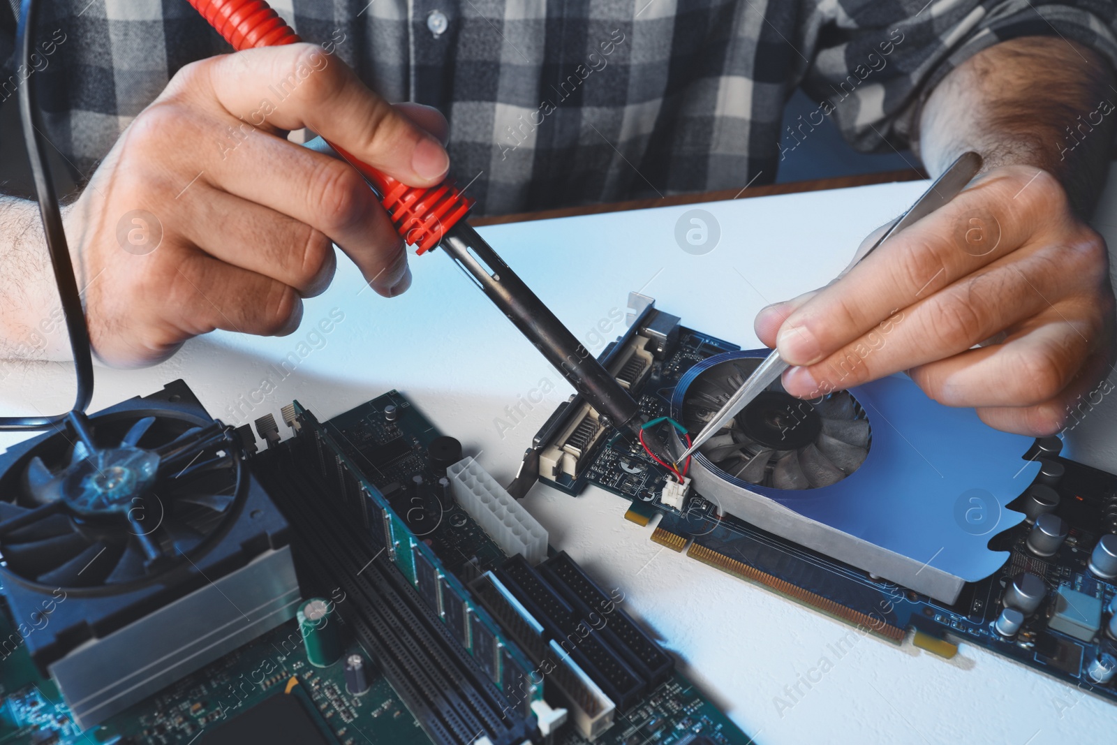 Photo of Technician repairing electronic circuit board with soldering iron at table, closeup