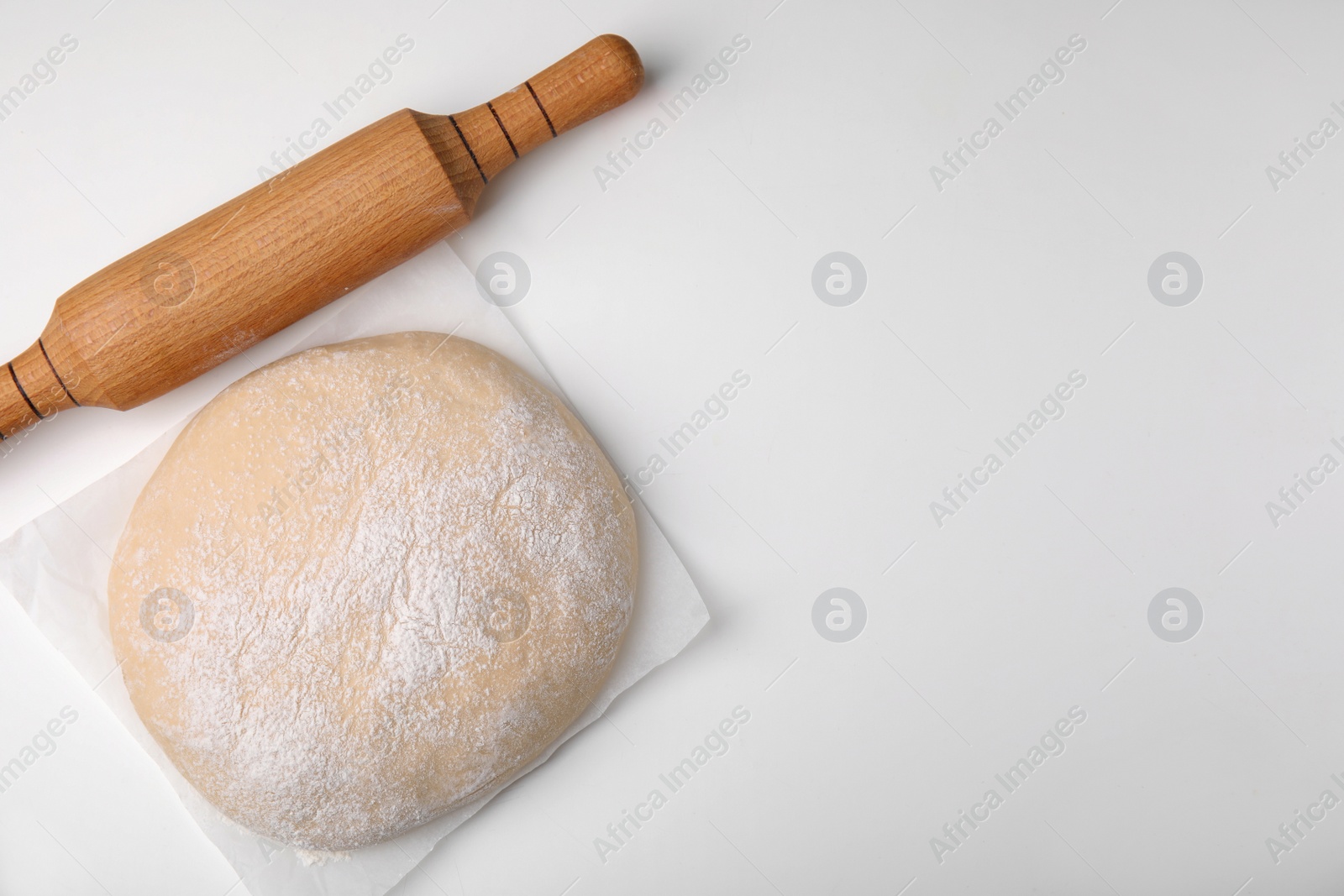 Photo of Fresh dough and rolling pin on white table, top view. Space for text
