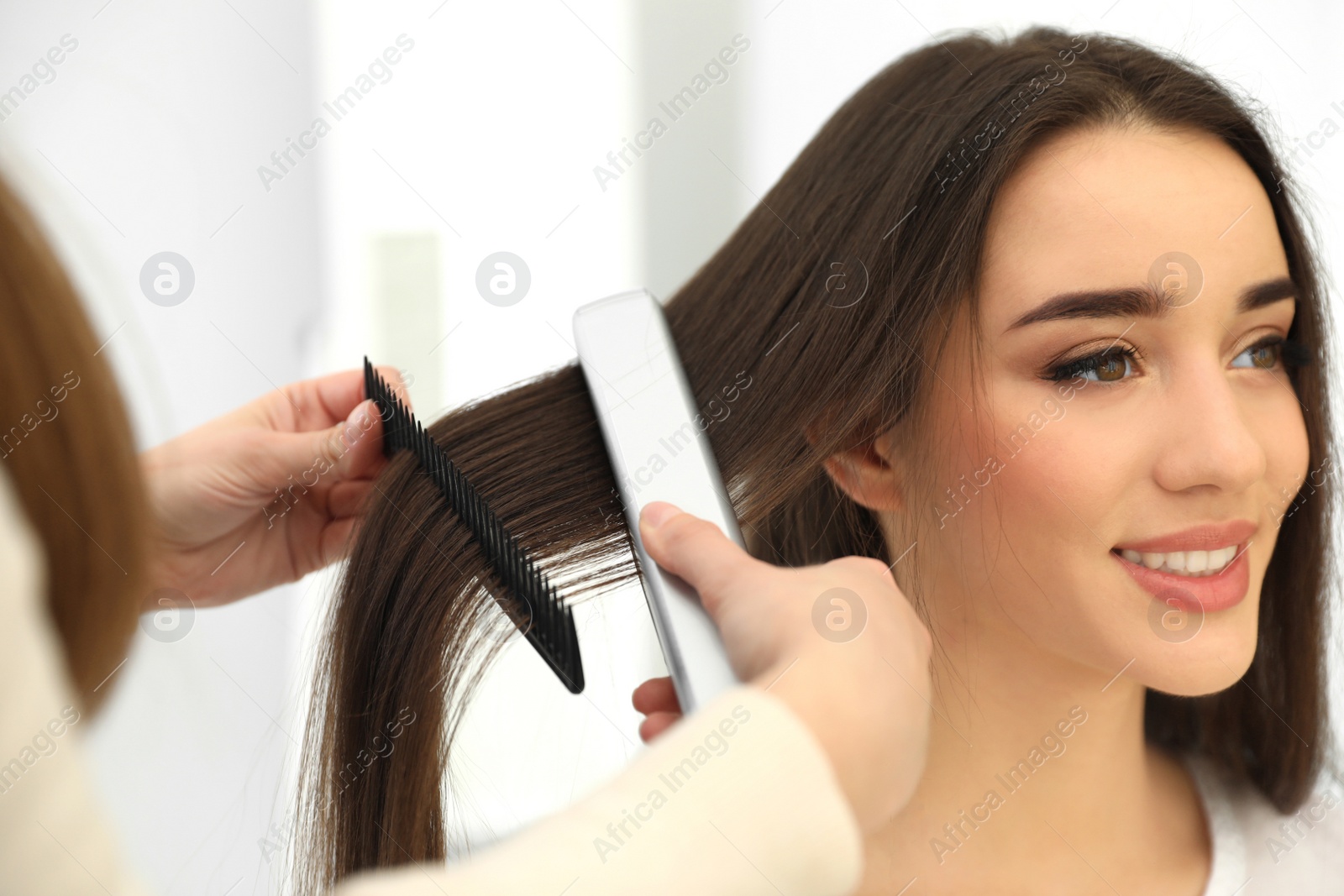 Photo of Hairdresser using modern flat iron to style client's hair in salon