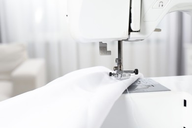 Photo of White sewing machine and fabric on blurred background, closeup