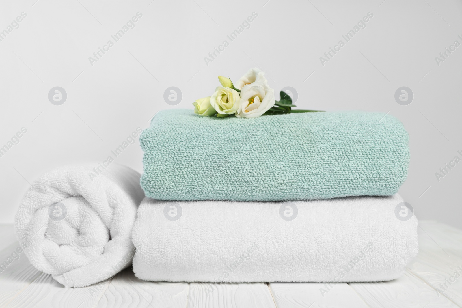 Photo of Soft towels with flowers on wooden table against white background