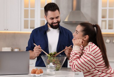 Happy lovely couple cooking together near laptop in kitchen