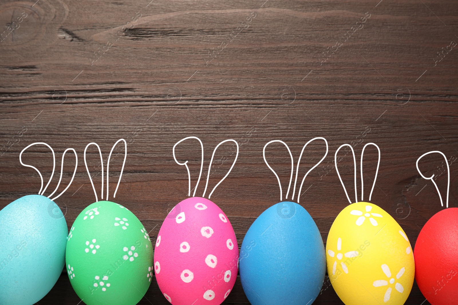 Image of Bright Easter eggs with cute bunny ears and space for text on wooden background, flat lay