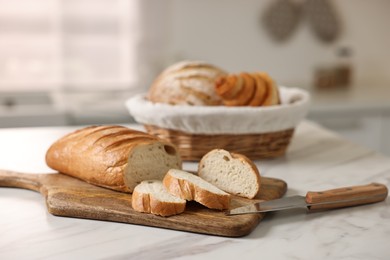 Photo of Wicker bread basket with freshly baked loaves and knife on white marble table in kitchen