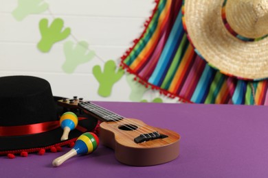Photo of Black Flamenco hat, ukulele and maracas on purple table. Space for text