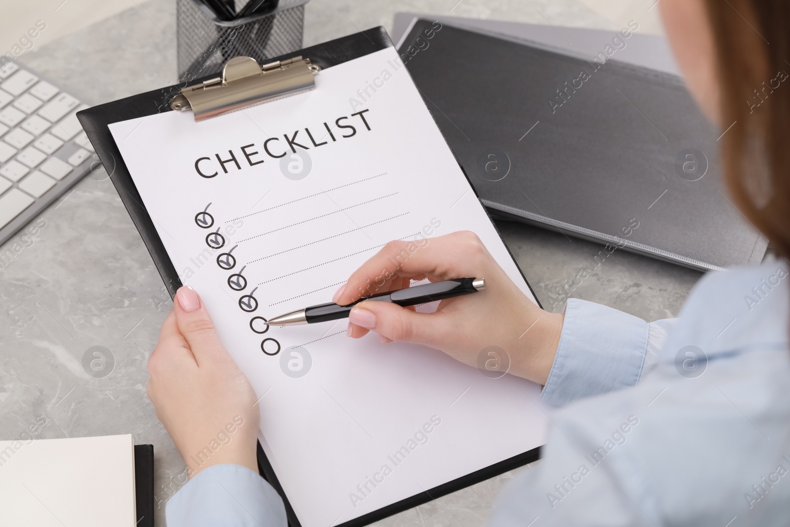 Photo of Woman filling Checklist at grey marble table, closeup