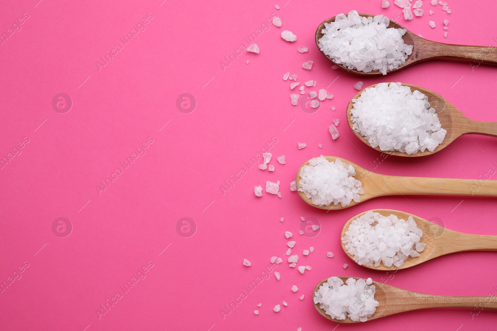 Photo of Spoons with sea salt on pink background, flat lay. Space for text