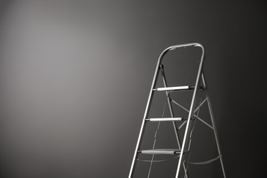 Modern metal stepladder against grey background. Space for text