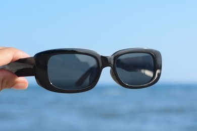 Woman holding stylish sunglasses near sea, closeup