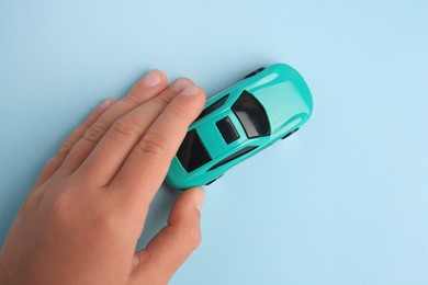 Child playing with toy car on light blue background, top view
