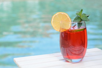 Photo of Glass of delicious cocktail on white wooden table near swimming pool, space for text. Refreshing drink