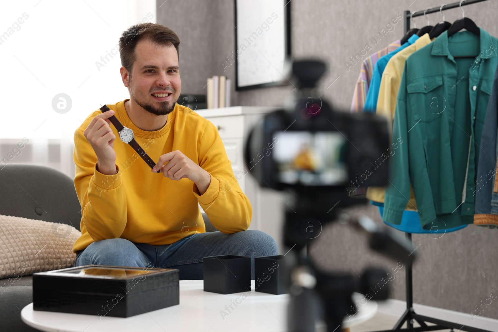 Photo of Smiling fashion blogger showing wristwatch while recording video at home