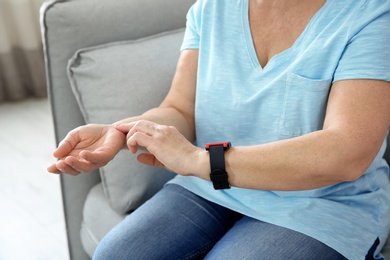 Photo of Mature woman checking pulse with fingers at home, closeup