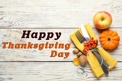 Happy Thanksgiving Day card. Top view of cutlery with napkin and autumn decor on white wooden table