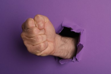 Photo of Man breaking through purple paper with fist, closeup