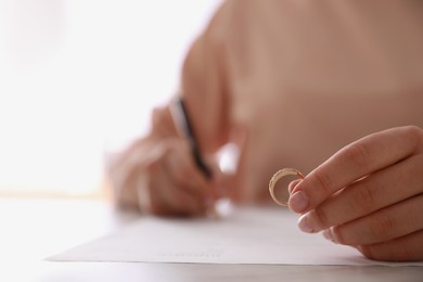 Photo of Woman with wedding ring signing divorce papers at table, closeup. Space for text