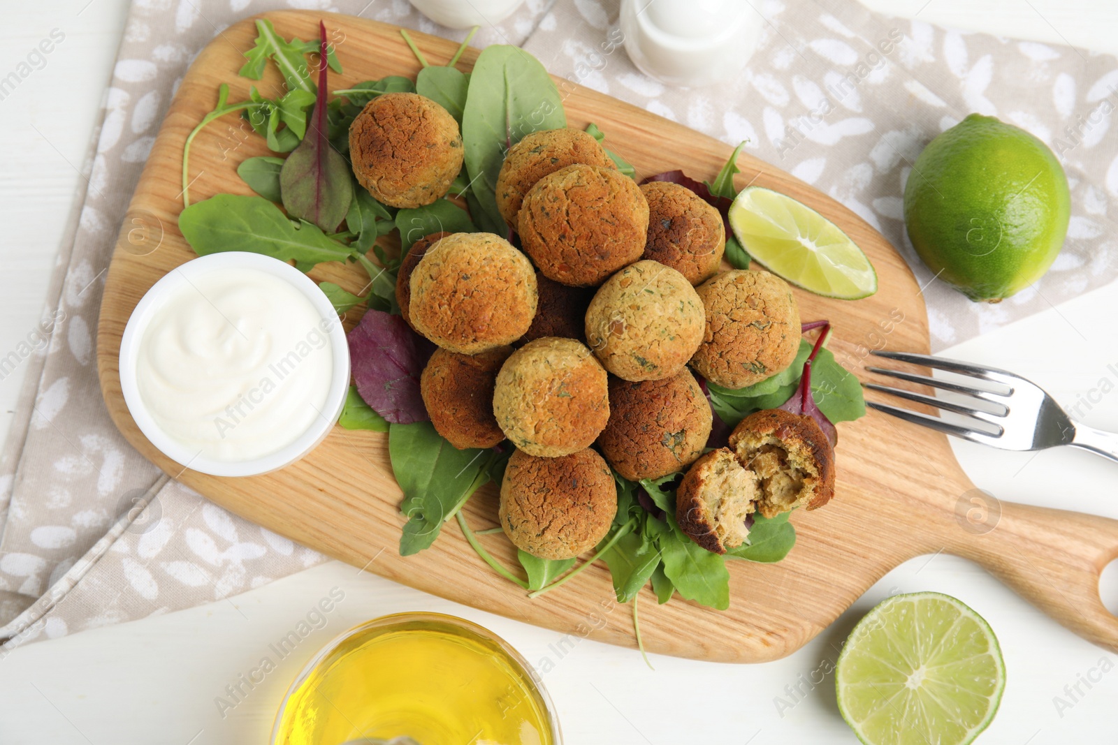 Photo of Delicious falafel balls with herbs, lime and sauce on white wooden table, flat lay