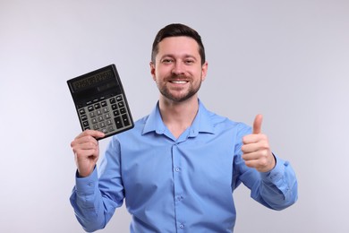 Photo of Happy accountant with calculator showing thumb up on light grey background