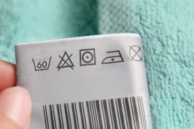 Woman holding clothing label on turquoise fluffy towel, closeup