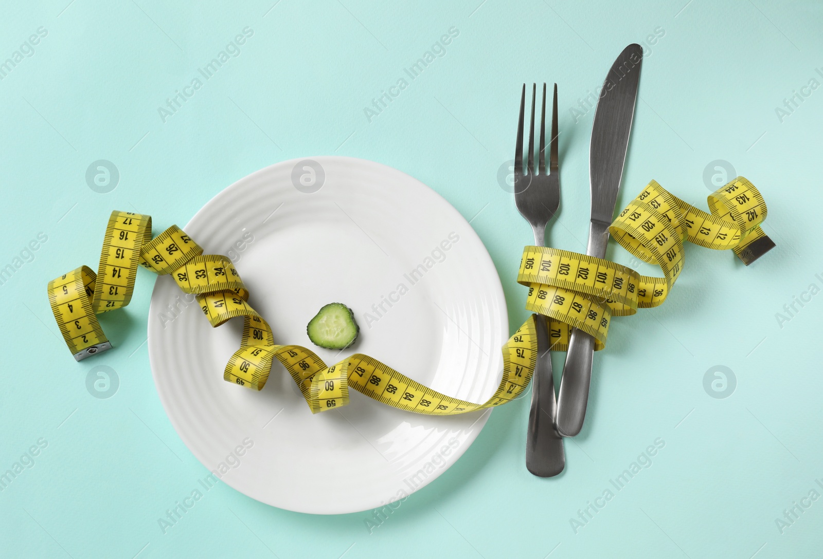 Photo of Plate with cucumber slice, cutlery and measuring tape on light blue background, flat lay. Diet concept