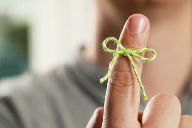 Photo of Man showing index finger with tied bow as reminder against blurred background, focus on hand