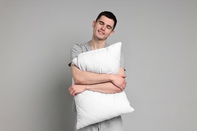 Happy man in pyjama holding pillow on grey background